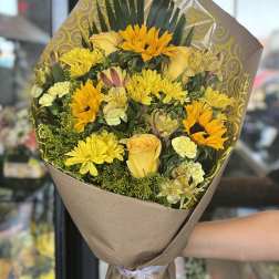 Yellow mixed bouquet wrapped in brown paper with a ribbon