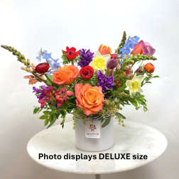 Bright mixed flower arrangement with orange roses, tulips, daffodils and other blooms in a white vase