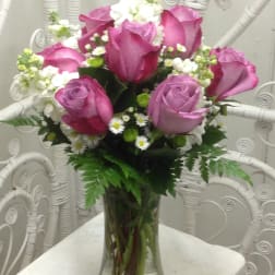 Pink and lavender roses arranged in a clear glass vase with white filler flowers.