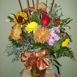 Mixed bouquet of sunflowers, roses, and chrysanthemums in a glass vase with a ribbon