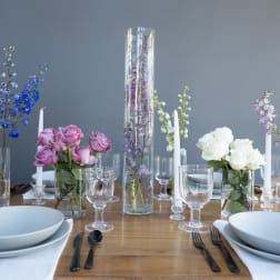 Table centerpiece with roses, delphinium, and tall glass cylinders