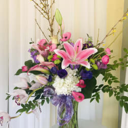 Pink lilies and mixed flowers in a glass vase with a purple ribbon