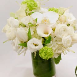 White floral arrangement in a glass vase with green accents