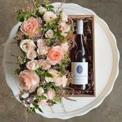 Pink and white rose arrangement beside a wine bottle in a gift box