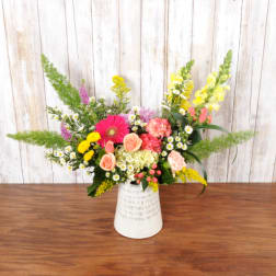 Asymmetrical mixed arrangement of pink, yellow and peach flowers in a white ceramic vase