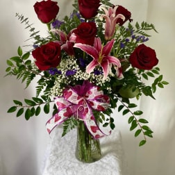 Red roses and pink lilies in a glass vase with a ribbon bow