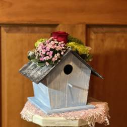 Small birdhouse topped with a red rose and pink flowers