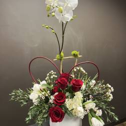 Red roses and white orchids in a white vase with heart-shaped accents
