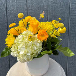 Yellow and white floral arrangement in a white vase with bee picks