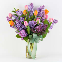 Bouquet of purple lilacs and pink tulips in a glass vase with a ribbon