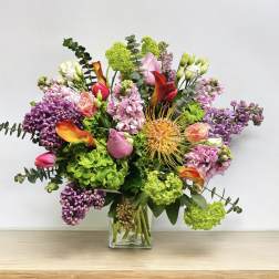 Mixed bouquet in a clear glass vase with pink, purple, green, and orange flowers
