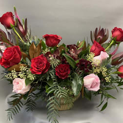 Red and pink roses arranged in a low basket with mixed foliage