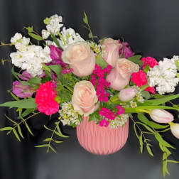 Pink and white roses arranged in a pink vase with greenery
