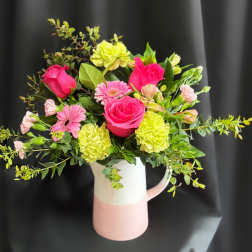 Pink roses and gerbera daisies in a white-and-pink pitcher vase
