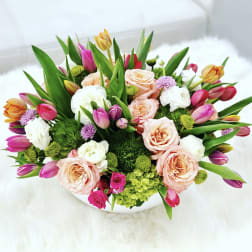 Mixed bouquet of pink, peach, white, and yellow flowers in a white container