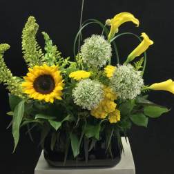 Yellow calla lilies and a sunflower in a black vase