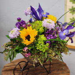 Mixed arrangement of sunflowers and purple irises in a small metal wheelbarrow container