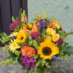 Bright mixed arrangement of sunflowers, roses, lilies and daisies in a clear glass vase