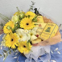 Yellow and white flowers arranged with bath and body gift items in a basket