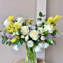 Bouquet of white roses and yellow filler flowers in a glass vase