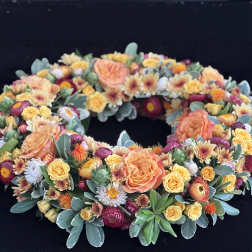 Circular floral wreath with peach, yellow, and burgundy blooms on a dark background