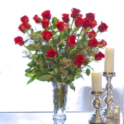 Red roses arranged in a clear glass vase beside white candles