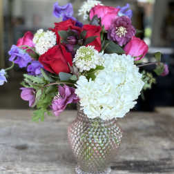 Bouquet of red roses, white hydrangea, and purple blooms in a textured vase