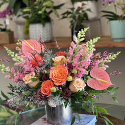 Colorful arrangement of peach roses, pink anthuriums, and snapdragons in a silver vase on books