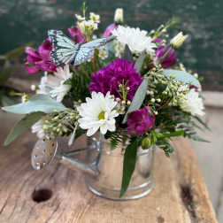Bouquet of white daisies and magenta flowers in a clear glass mug with a butterfly decoration