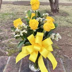 Yellow roses in a clear glass vase with a large yellow ribbon