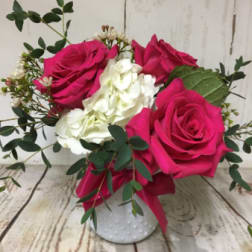 Small arrangement of hot pink roses and white hydrangea in a white textured vase with greenery.