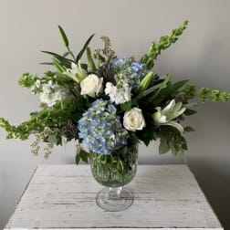 Large white and blue flower arrangement with lilies, roses and hydrangeas in a clear glass pedestal vase