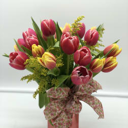 Pink and yellow tulips in a pink vase with a floral ribbon