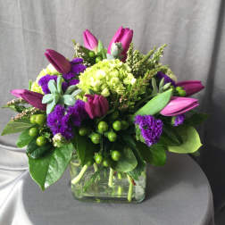 Mixed bouquet of purple tulips, green hydrangea, and a glass vase
