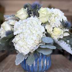 White hydrangeas and pale roses in a blue glass vase