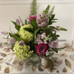 Spring arrangement with green hydrangeas, pink roses, and tulips in a glass vase beside a bunny figurine.