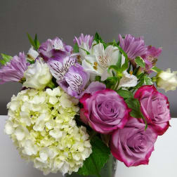 Bouquet of purple roses, white lilies, and pale hydrangea in a glass vase
