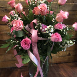 Pink roses and small white daisies in a glass vase with pink ribbon