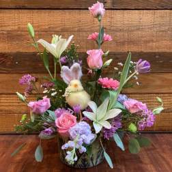Pink and white floral arrangement with a small bunny decoration in a patterned container
