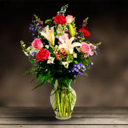Mixed bouquet of lilies, roses, carnations, and purple daisies in a glass vase