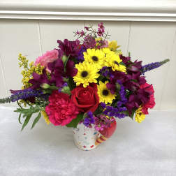 Bright mixed flower arrangement in a colorful patterned mug-style container