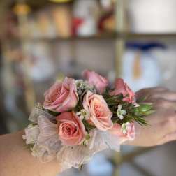 Peach-pink rose wrist corsage with small white blossoms and sheer ribbon on a person's arm