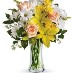 Bouquet of yellow lilies, peach roses, and white daisies in a clear glass vase