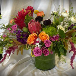 Mixed bouquet in a green glass vase with orange, pink, purple, and white blooms