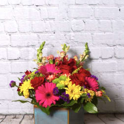 Bright mixed flower arrangement in a square blue vase