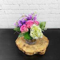 Pink roses and purple flowers arranged in a small glass vase