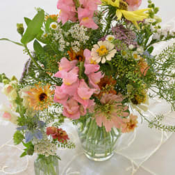 Mixed pastel flower arrangements in clear glass vases on a white tablecloth