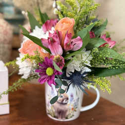 Mixed bouquet in a printed mug vase with pink, peach, and white flowers