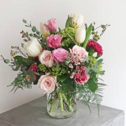 Bouquet of pink roses, white tulips, and carnations in a glass vase