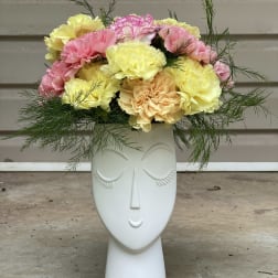 Pastel carnations arranged in a white face-shaped vase